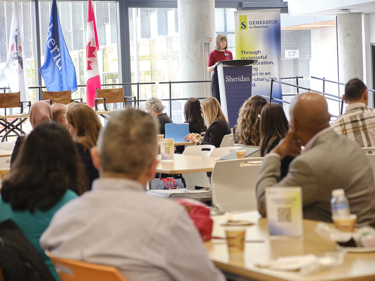People seated at tables looking at a person behind a podium who is speaking