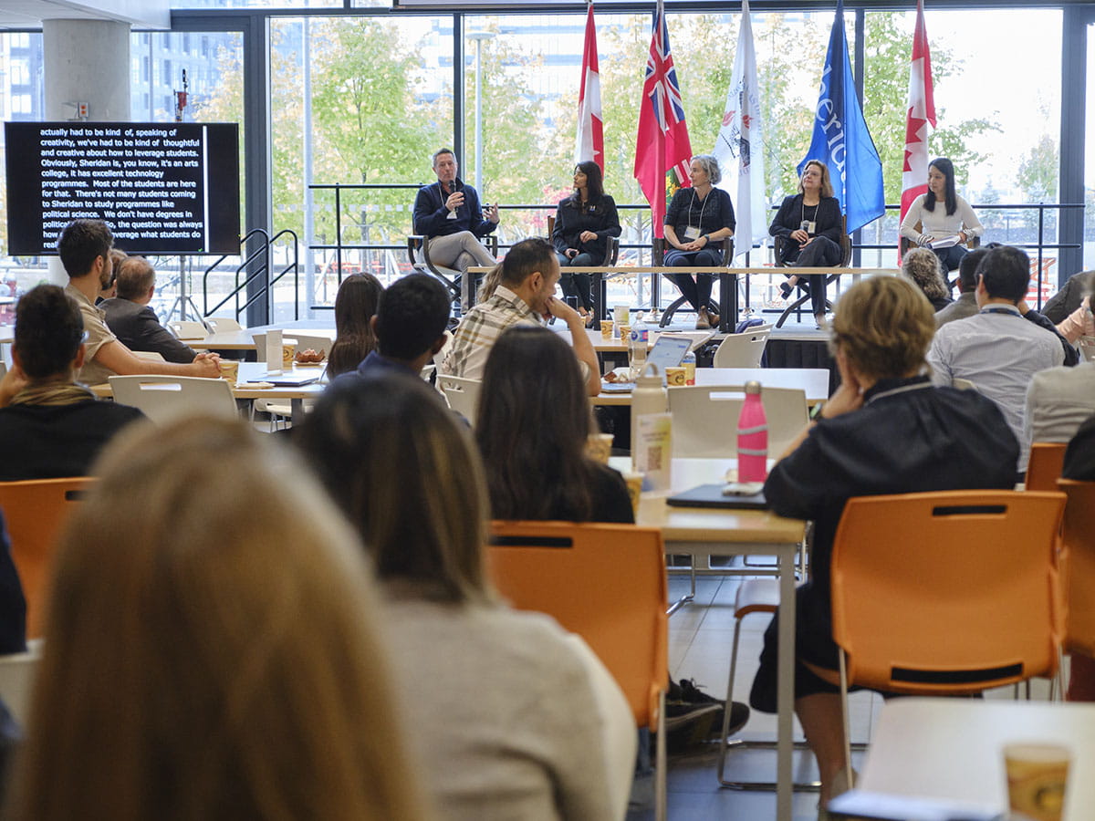 People seated at tables looking at a group of people on stage sitting side-by-side