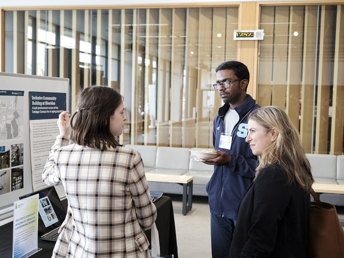A person talks to two others while gesturing to a display board