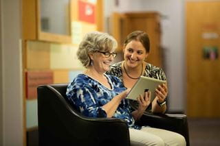 A Sheridan researcher holding a tablet device for a senior to look at