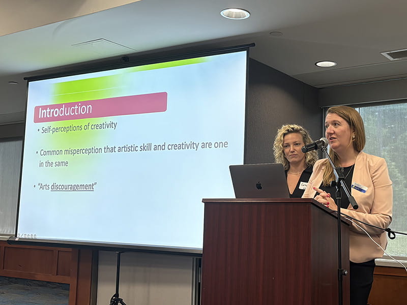 A person standing at a podium with a screen beside them.