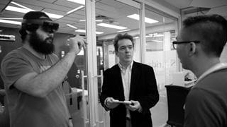 Three people in discussion. One is wearing a VR headset.