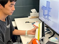 Person measuring a piece of framing while seated in front of a computer monitor