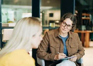 Person seated with a pen and paper looking at a person sitting next to them