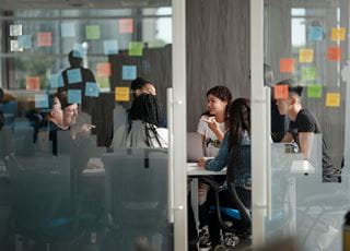 A group of students talking in a room with colourful sticky notes on the wall.
