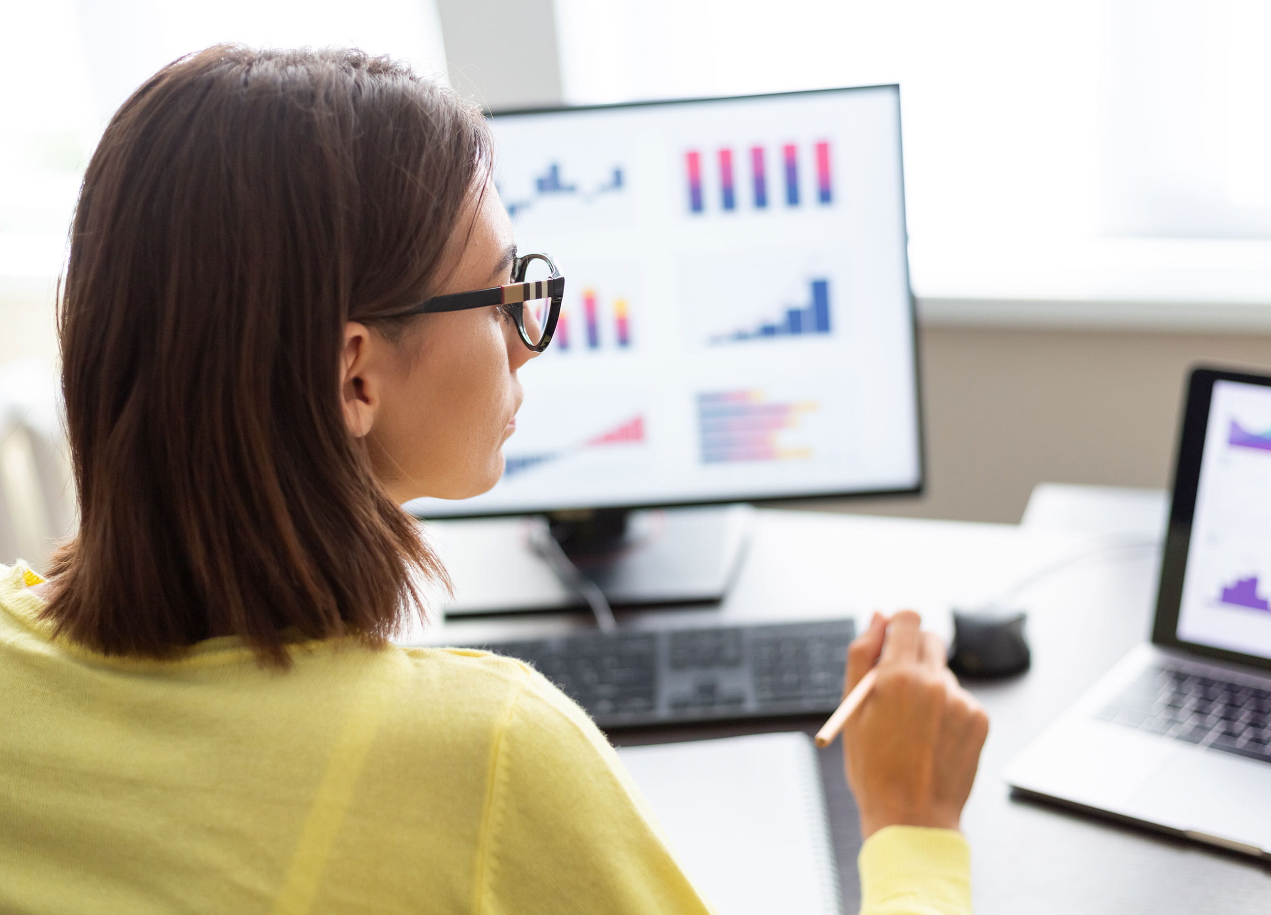 A person looking at data graphs on two computer monitors.