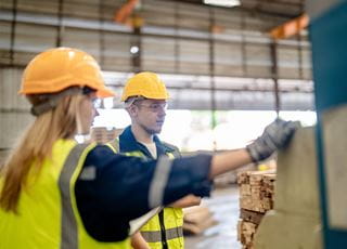 Two people wearing hard hats working with lumber