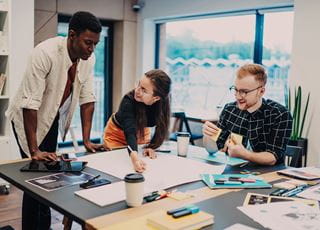 Three students working collaboratively at a table with poster paper and sticky notes.
