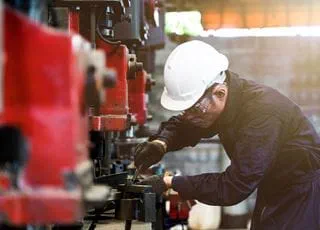 A person wearing a hard hat and coveralls working with industrial machinery.