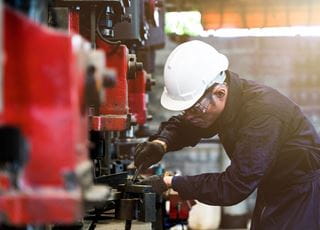 A person wearing a hard hat and coveralls working with industrial machinery.