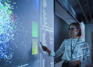 Person in front of a projected screen pointing to an item on it using a pen