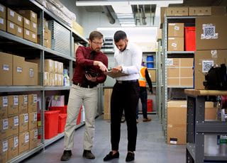 Two people in business attire making notes on a clipboard in a warehouse storage room