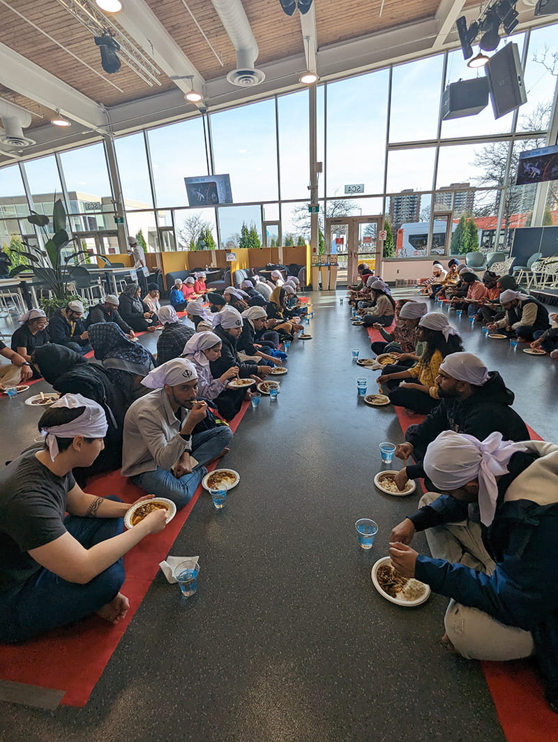 People seated on the floor in two rows across from eachother, eating a meal