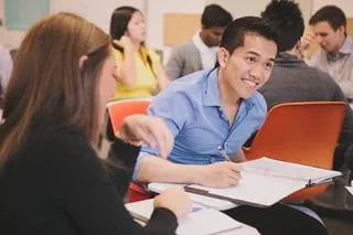 Students writing in notebooks at tables in a classroom