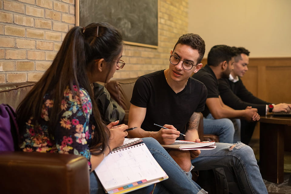 Two students having a discussion as they sit on a sofa studying.