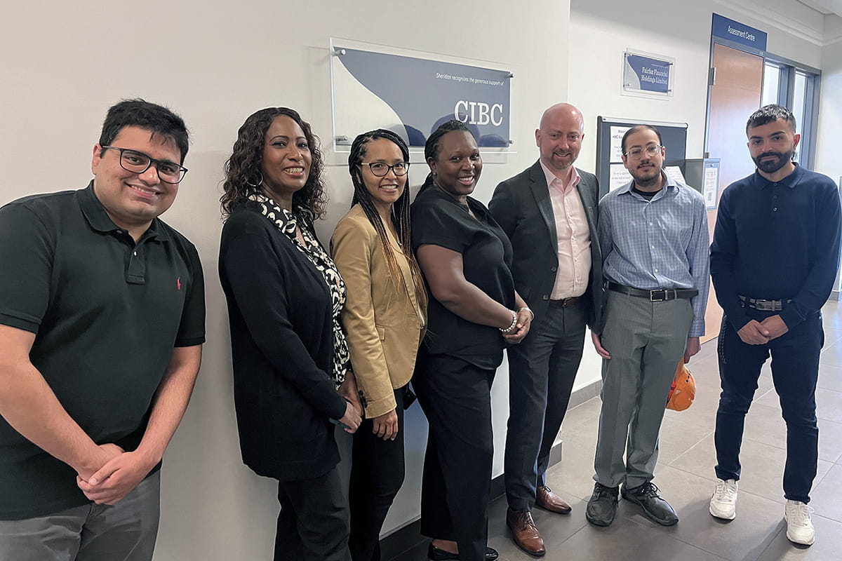 Seven people posing side-by-side in front of a CIBC wall plaque