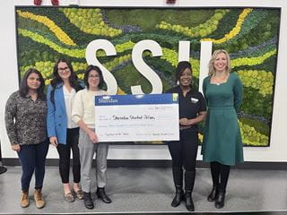 Five people posing with a large cheque